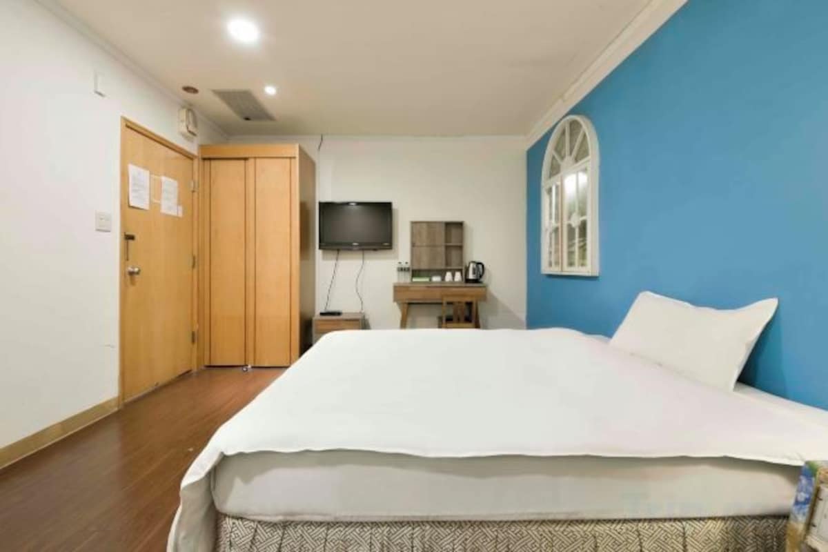 A hotel room with a bed, a television, a desk with a computer, and a window.
