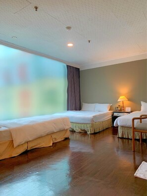 Habitación de hotel con dos camas individuales, suelo de madera, mesita de noche con lámpara y ventana con cortinas.