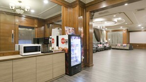 A hotel lobby with a reception desk, a microwave, a refrigerator, and a seating area with sofas and a chandelier. - Back Home Hotel (Chiayi City)