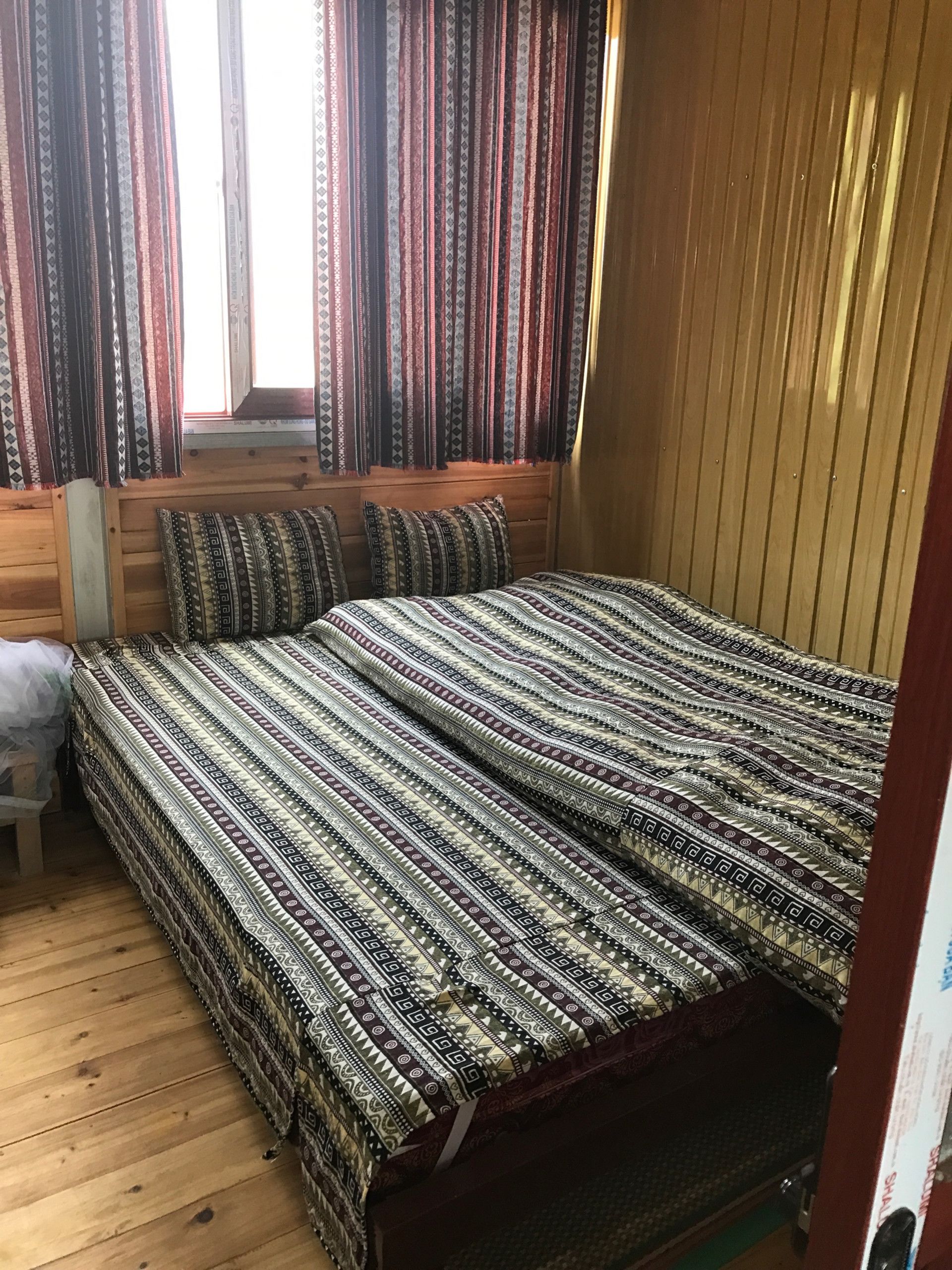A wooden-paneled room with a bed, pillows, and curtains.