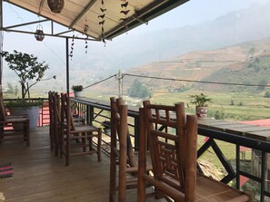 A wooden deck with chairs and potted plants, overlooking a hilly landscape. - Moc Anh House (Ta Van)