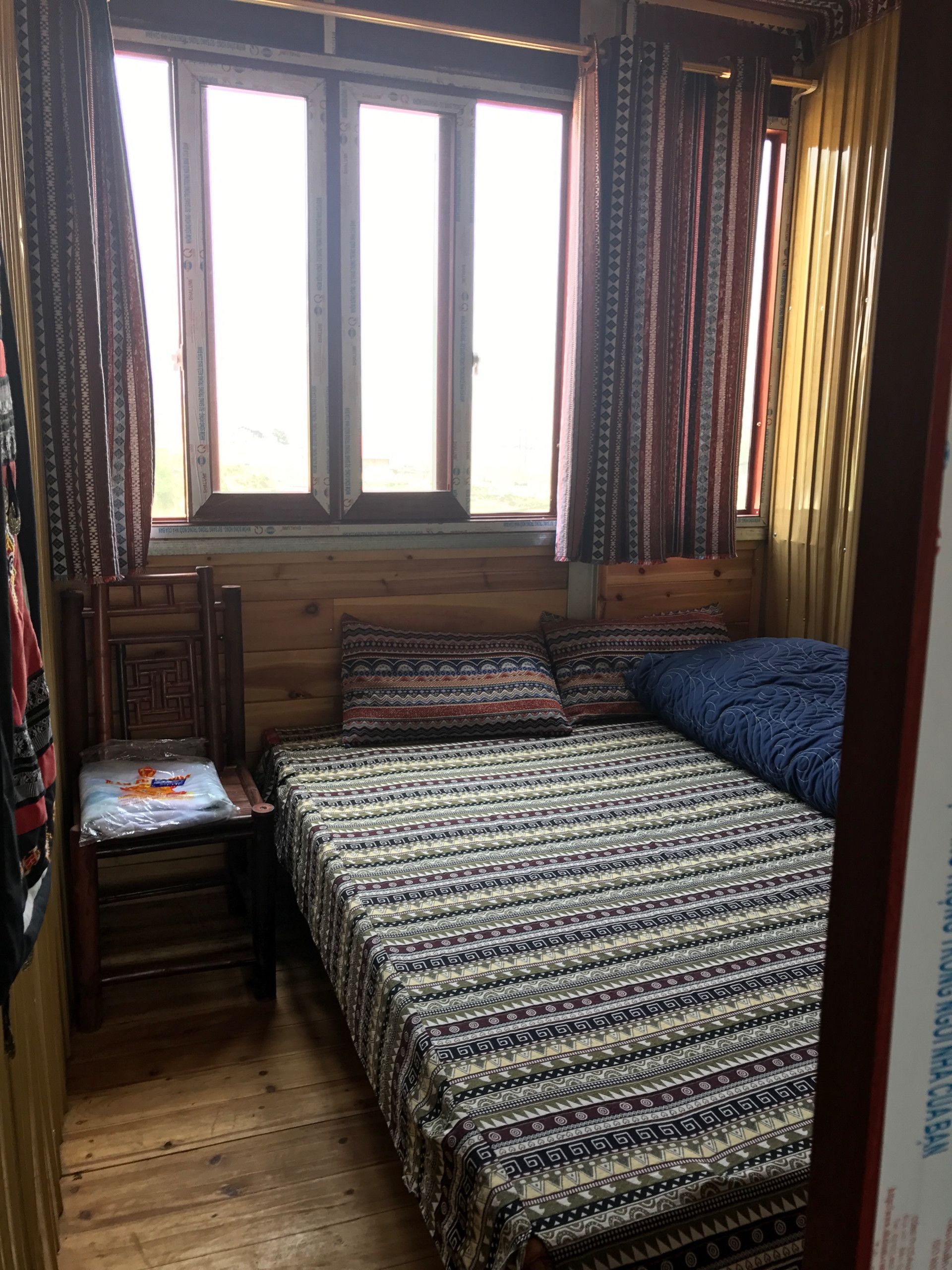 Een kleine, gezellige kamer met een houten bed, een stoel en een raam met gordijnen.