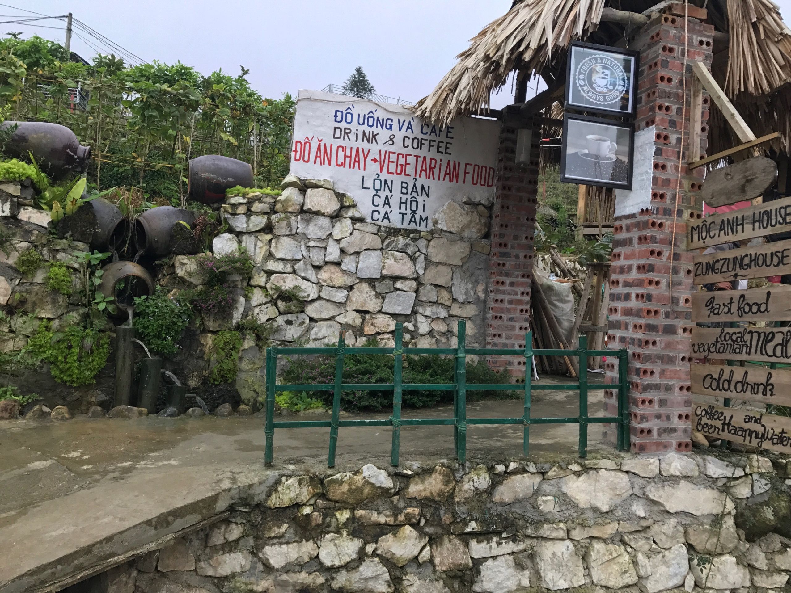 A rustic building with a stone wall and a signboard advertising a cafe and vegetarian food.