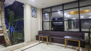 Una hall con un divano dai toni scuri, due tavolini, un'ampia finestra e un murale raffigurante una scena tropicale.