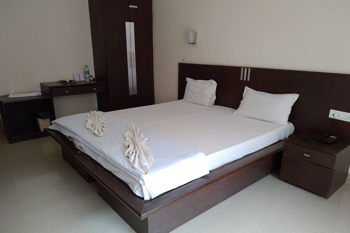 A hotel room with a large bed, a bedside table with a phone, a nightstand, and a wardrobe.