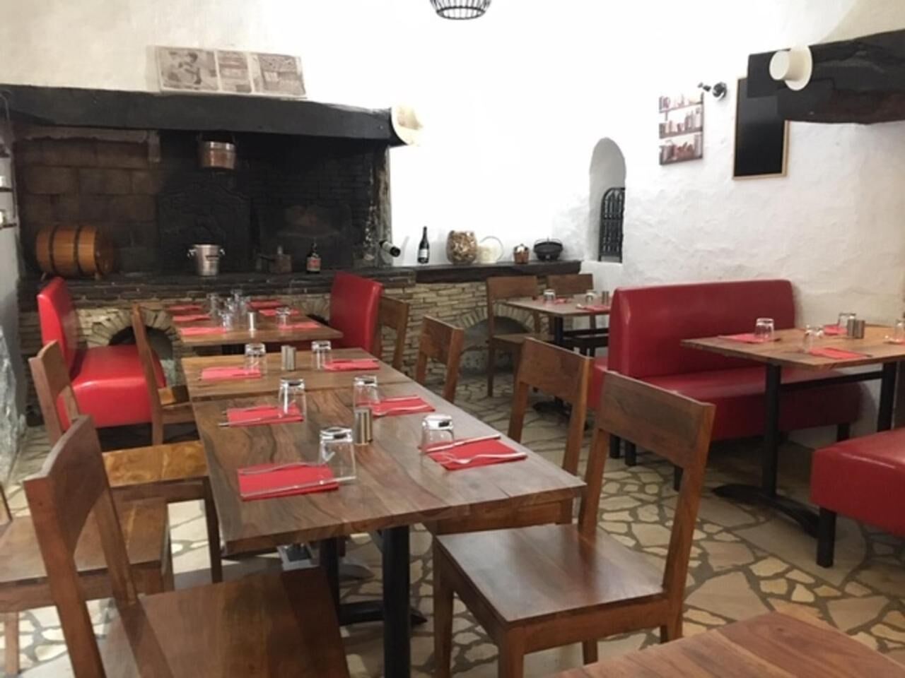 Un restaurante con mesas de madera, asientos tapizados en rojo y una chimenea de piedra, además de un suelo de baldosas.
