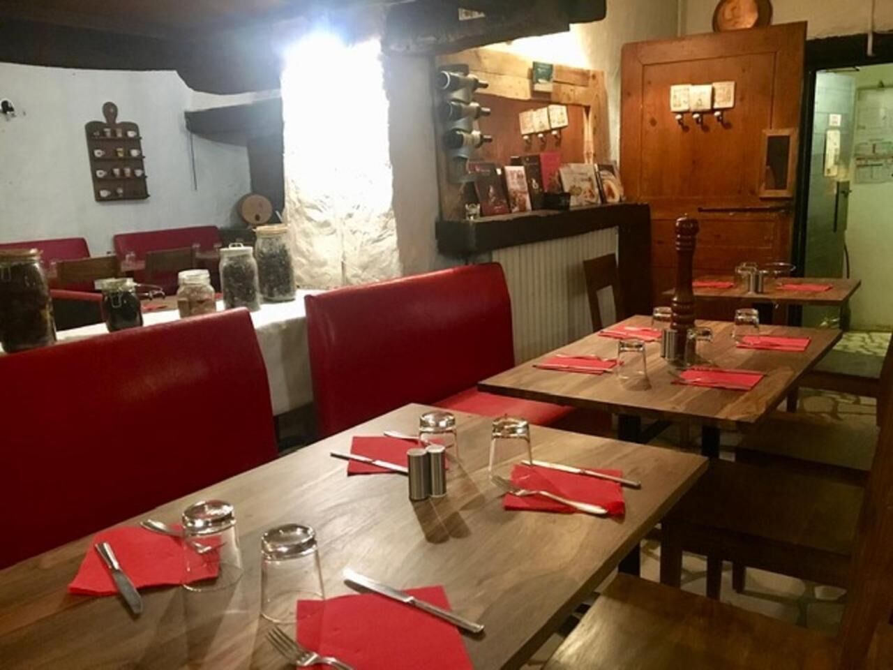 Un restaurante con mesas de madera y sillas rojas, provisto de cubiertos y aderezos.