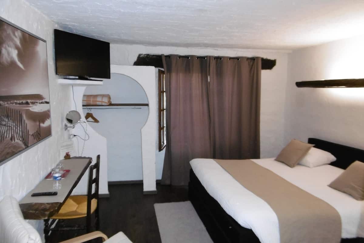 Une chambre d’hôtel équipée d’un lit, d’un bureau, d’une chaise, d’une télévision et d’une fenêtre avec des rideaux.