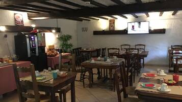 Un restaurant avec des tables et des chaises en bois, un appareil à café et un écran de télévision fixé au mur.