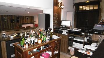 A bar area with a wooden counter, various bottles, glasses, and a computer monitor.