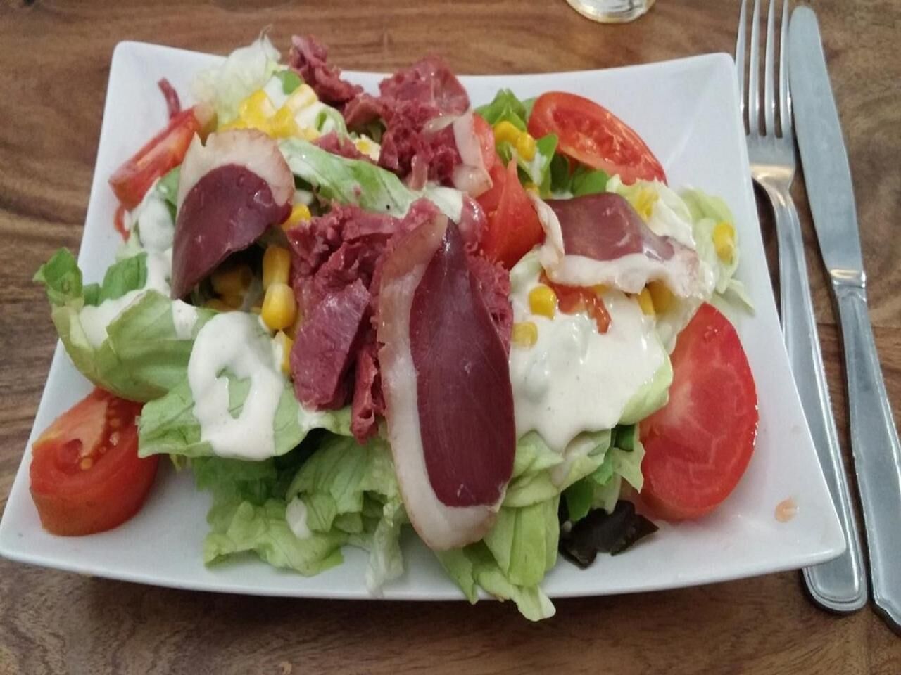 A plate of mixed greens salad with bacon, corn, and tomatoes.