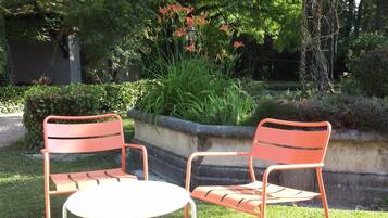 An outdoor seating area with two metal chairs and a small round table, surrounded by lush greenery and trees.