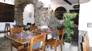 A restaurant interior with stone walls, wooden tables and chairs, and a large potted plant. - Relais Des Vieilles Postes (Les Avenieres-Veyrins-Thuellin)