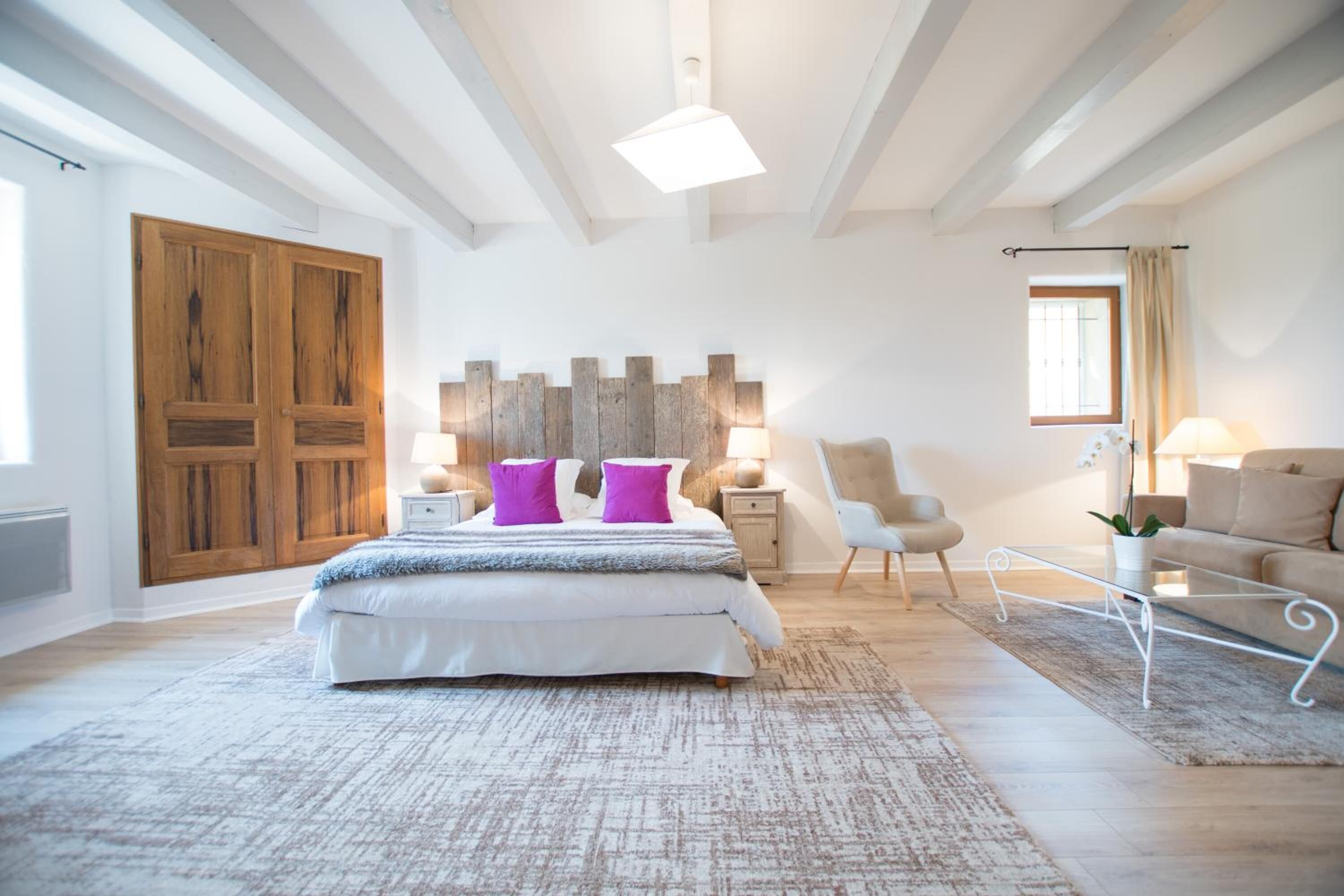 Un dormitorio espacioso con una cama grande, armario de madera, una silla moderna y un sofá.