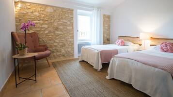 Un dormitorio con dos camas, una silla, una mesita y una pared de piedra.