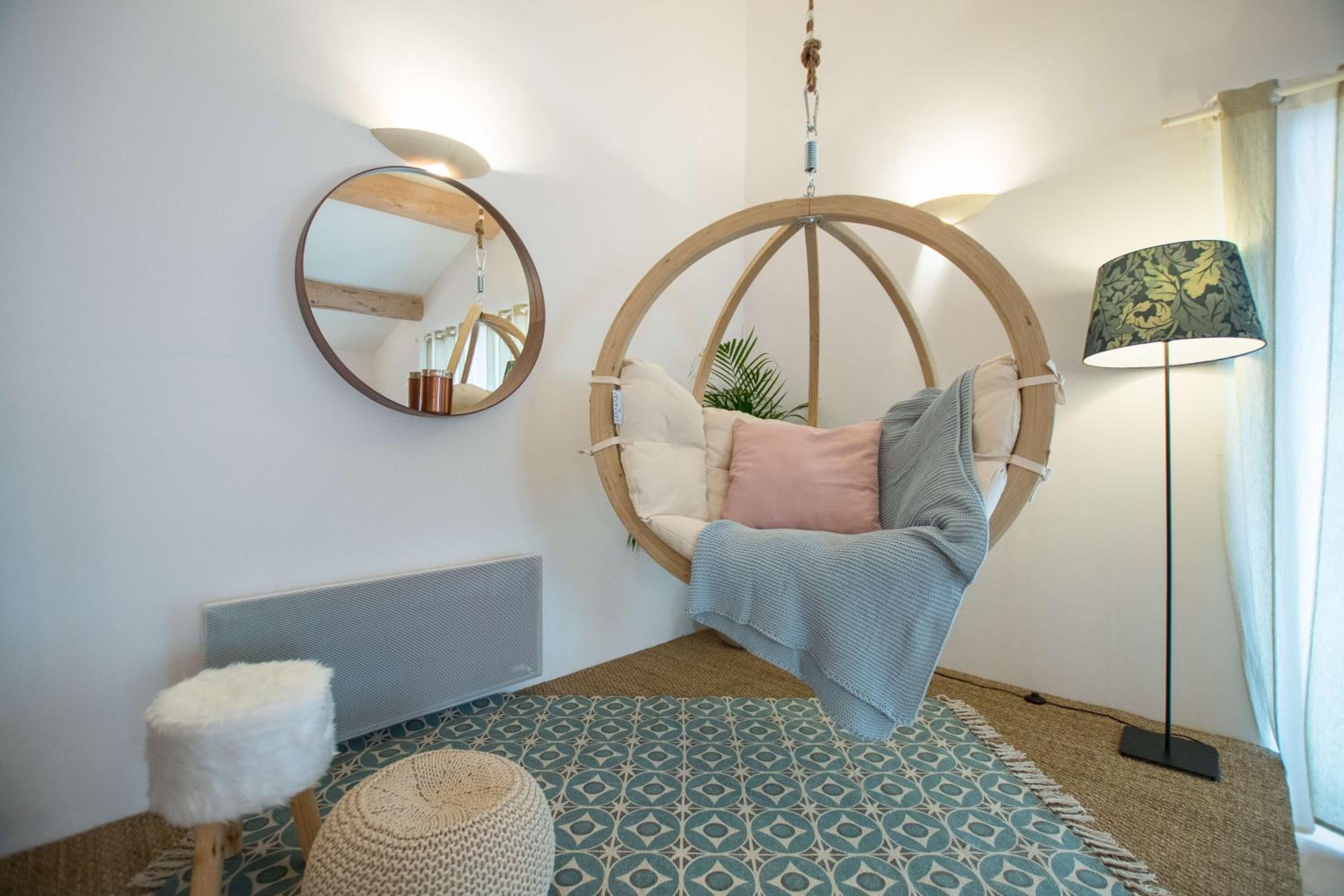A cozy room with a hanging chair, a round mirror, a floor lamp, and a patterned rug.