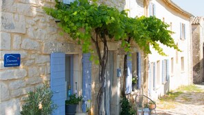 A stone building with a small garden area, a table with goods, and a sign indicating a local product. - La Bastide des Bourguets (Sault)