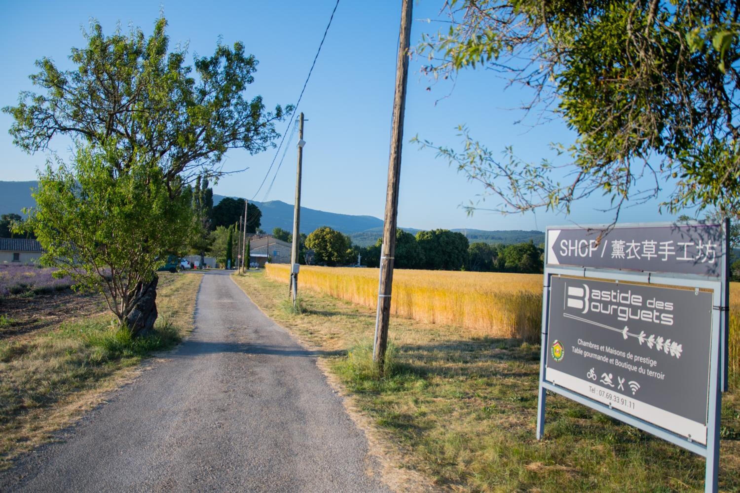 Eine Landstraße mit einem Schild für 'Bastide des Bourguets' und einer Kontaktnummer.