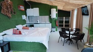 Hotelkamer met een bed, een kleine kitchenette, een zithoek met een tafel en stoelen, en een groene wand.
