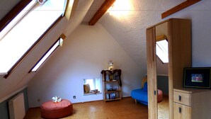 A loft-style room with a sloped ceiling, wooden beams, a red bean bag, a blue sofa, a wooden cabinet, and a small window with a view. - Relaxen am Nationalpark Eifel (Blankenheim)