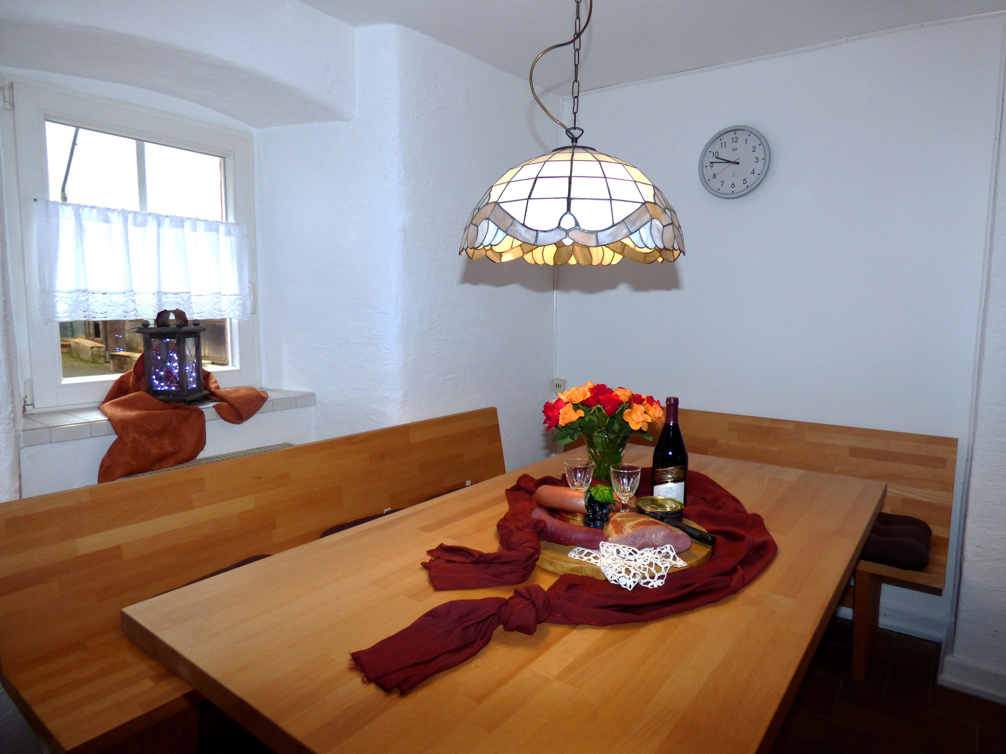 A dining area with a wooden table, a chandelier, a clock, and a window with curtains.