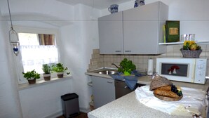 A compact kitchen with white cabinets, a microwave, a sink, and a window with potted plants. - Relaxen am Nationalpark Eifel (Blankenheim)