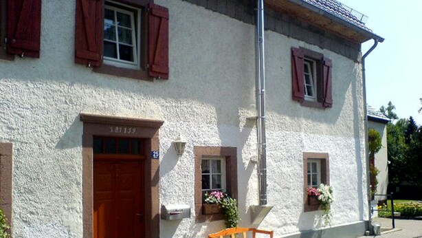 A white building with a wooden door and windows with red shutters. There is a bench and potted plants outside. - Relaxen am Nationalpark Eifel (Blankenheim)