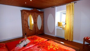 A room with wooden ceiling and walls, a bed with red floral bedding, a wooden wardrobe, and a window with yellow curtains. - Relaxen am Nationalpark Eifel (Blankenheim)