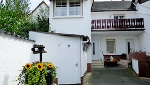 A white house with a front door, a small balcony, and a garden with a sunflower planter. - Relaxen im alten Winzerhaus (Rech)