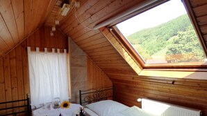 A cozy wooden cabin room with a bed, a small table with a sunflower, and a window overlooking a forested hillside. - Relaxen im alten Winzerhaus (Rech)