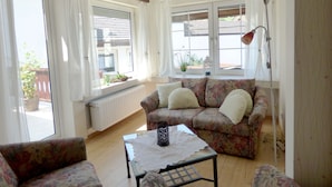 A cozy living room with a floral sofa, a small table with a lace tablecloth, and a floor lamp. - Relaxen im alten Winzerhaus (Rech)
