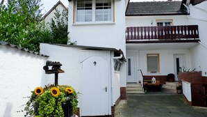 Une maison blanche avec une porte blanche, un petit jardin avec des tournesols et une clôture en bois.