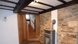 A room with a stone wall, a wood-burning stove, a wooden staircase, and a door leading to another room. - Relaxen im gemütlichen Eifelhaus (Kesseling)