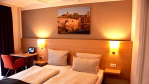 A hotel room with a bed, two bedside tables, a desk with a chair, and a painting of a bridge on the wall. - Altes Eishaus, Hotel & Restaurant (Giessen)
