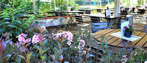 An outdoor seating area with tables and chairs, surrounded by greenery and flowers.