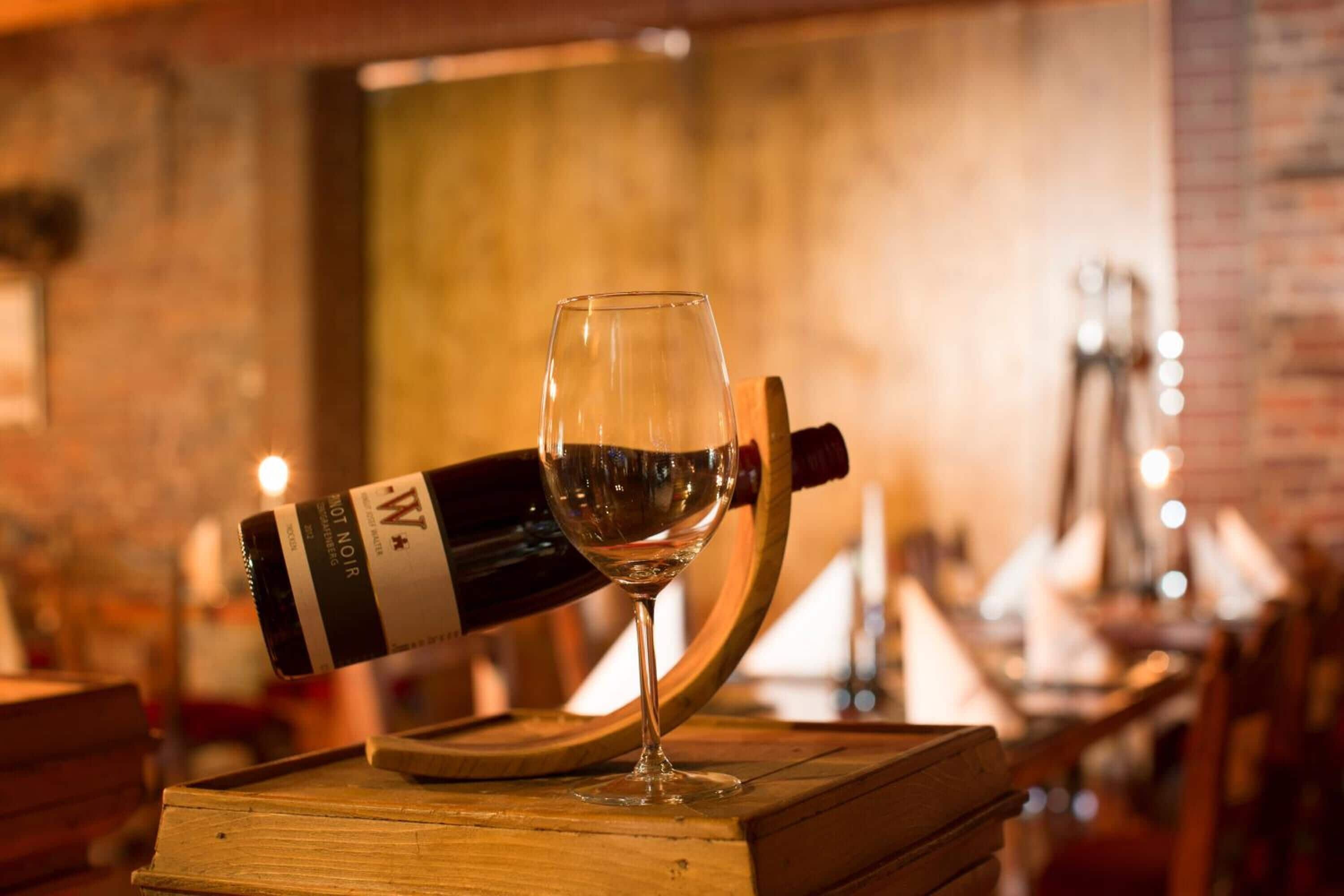 Una botella de vino volcada con una copa sobre una mesa de madera en un restaurante.