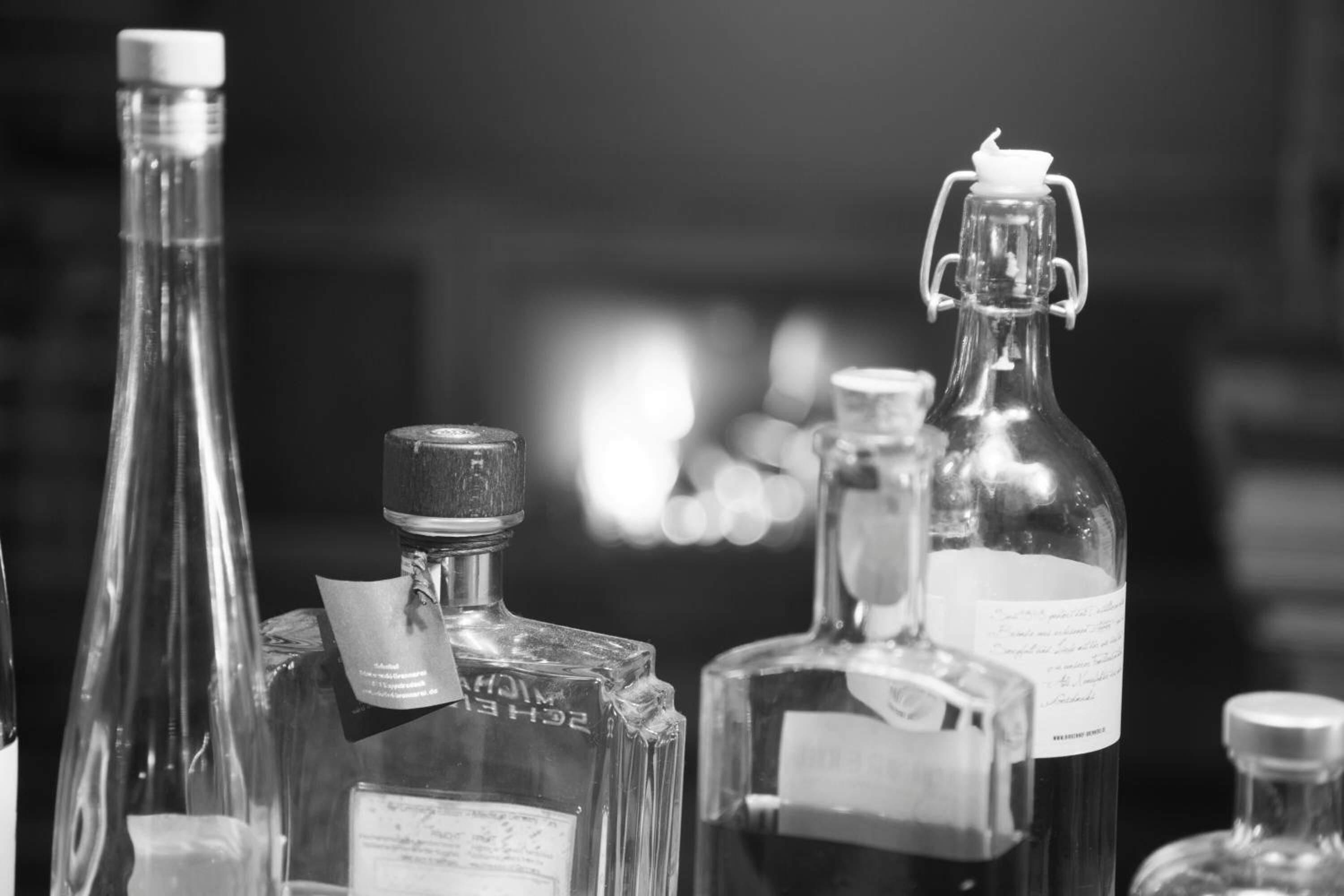 A collection of clear glass bottles with labels, some with corks, and a few with metal caps, arranged closely together.