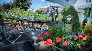 An outdoor seating area with tables and chairs, surrounded by potted plants and flowers.