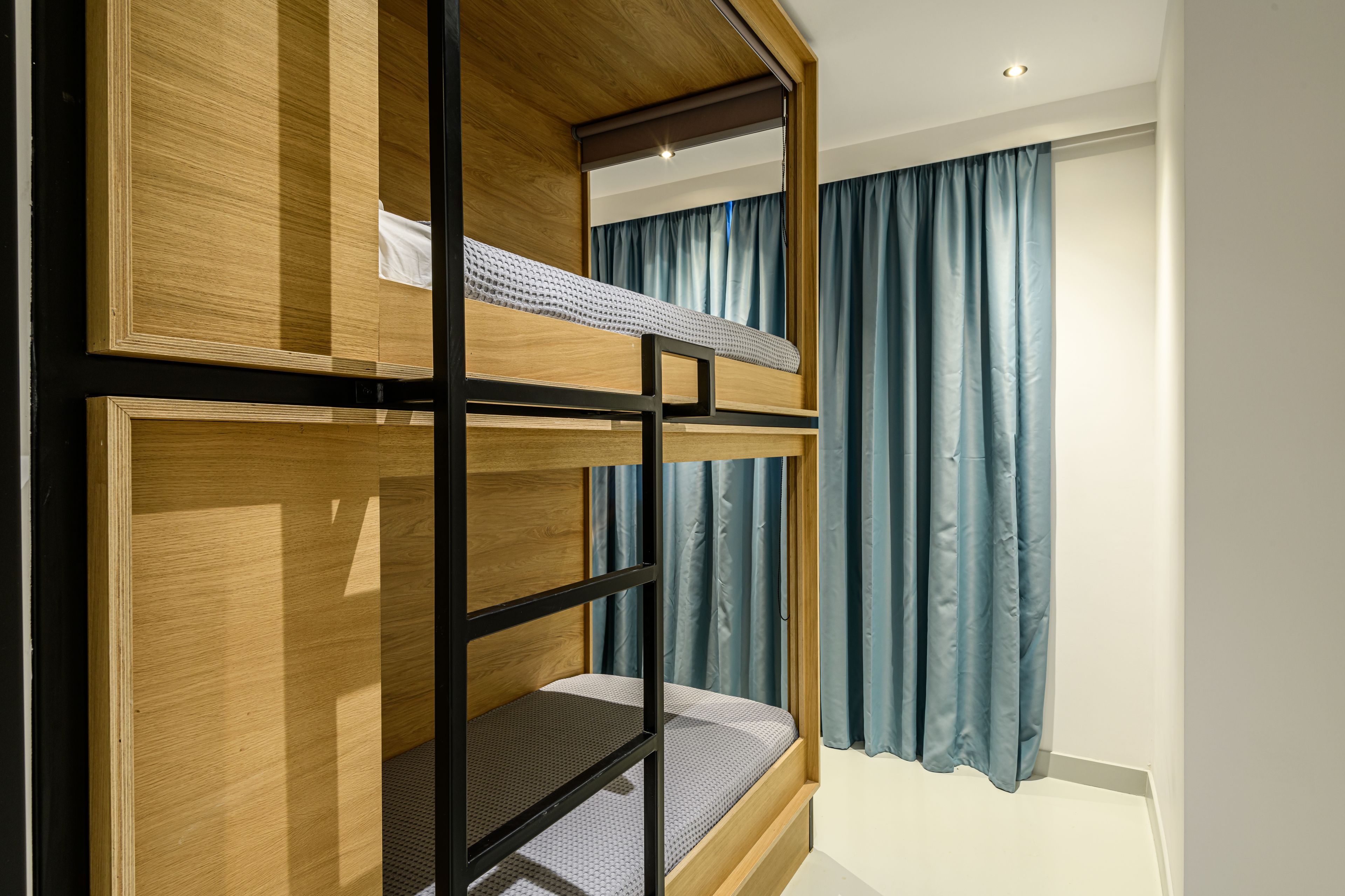 A bunk bed room with wooden frames and a window with blue curtains.