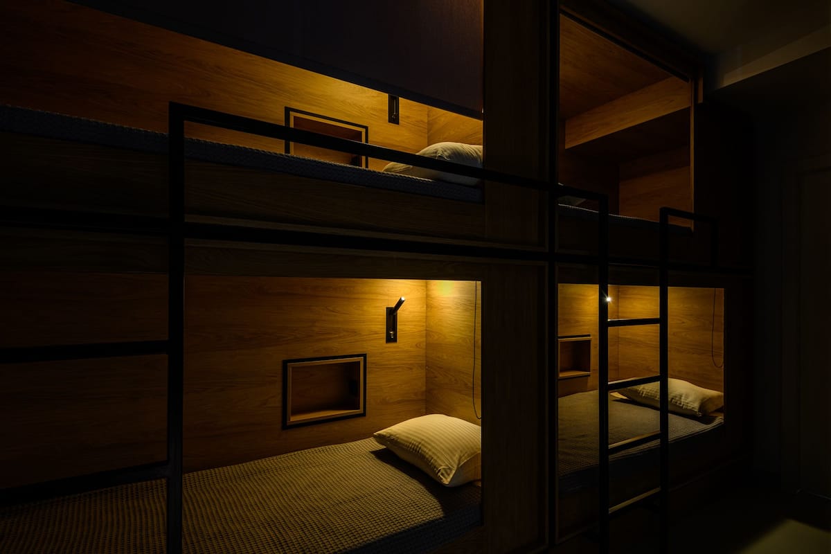 A bunk bed room with wooden walls and a single bedside table.