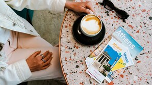 A table with a coffee cup, sunglasses, and travel brochures. - Mosaikon - Hostel (Athens)