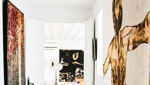 A hallway with a patterned rug, a large abstract painting on the left, and a wooden sculpture on the right.