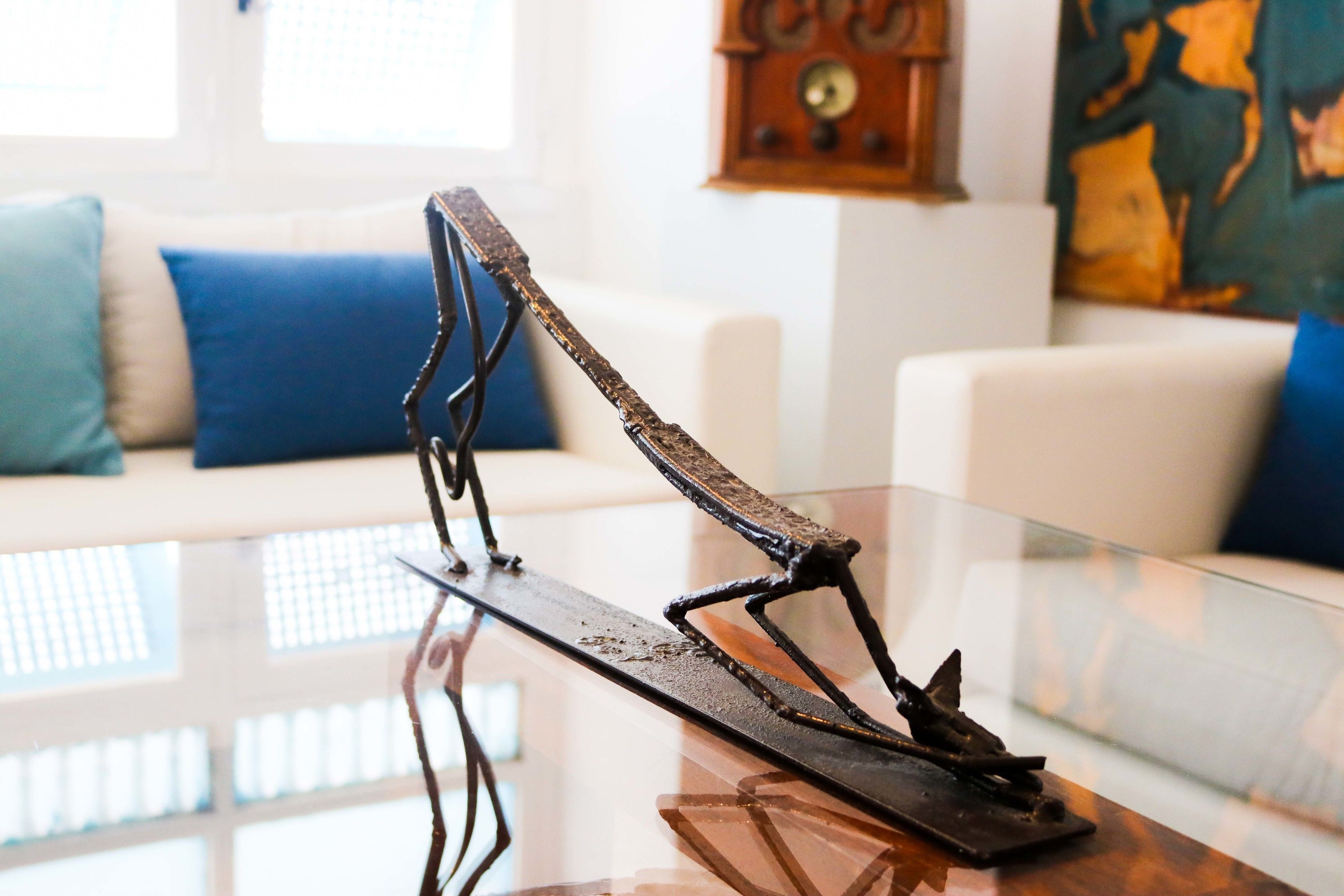 Una sala moderna con una mesa de centro de vidrio, un sofá blanco con cojines azules y un reloj de pared.