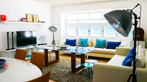 A living room with a TV, a glass-top coffee table, a sofa with blue cushions, and a floor lamp.