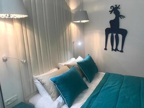 A hotel room with a bed, teal pillows, a wall-mounted giraffe decoration, and two pendant lights.