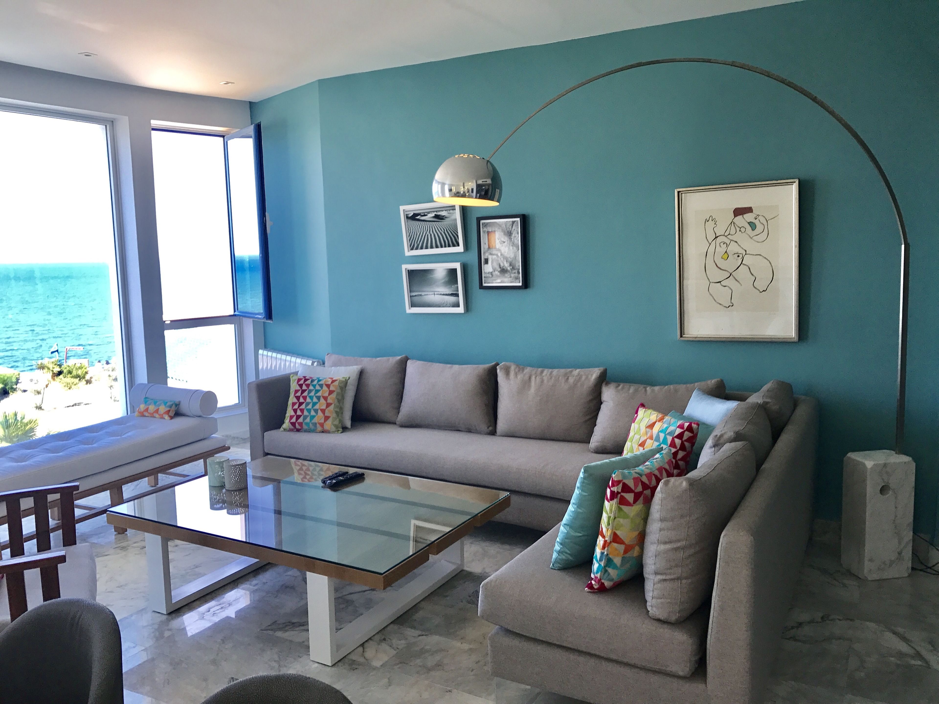 A modern living room with a sofa, a glass coffee table, and a view of the ocean.