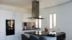 A modern kitchen with white cabinets, a black stove, and a central island with bar stools. - The View (La Marsa)