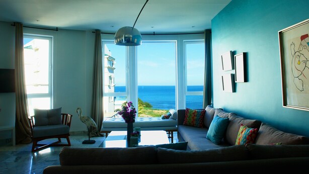 A living room with a large window offering a view of the ocean, a sofa, a chair, and a table with a vase. - The View (La Marsa)