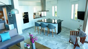 A modern kitchen with a central island, a dining area with chairs, a sofa, and a coffee table with flowers. - The View (La Marsa)