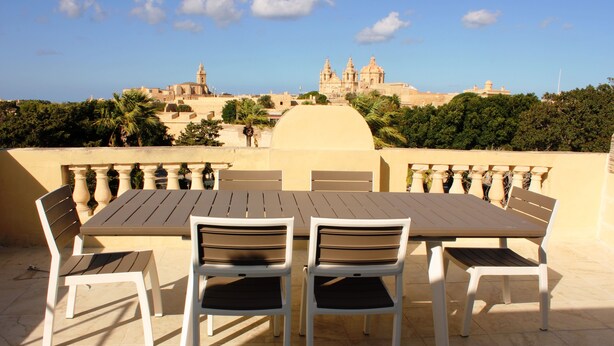 An outdoor terrace with a table and chairs, overlooking a historic building with domes.